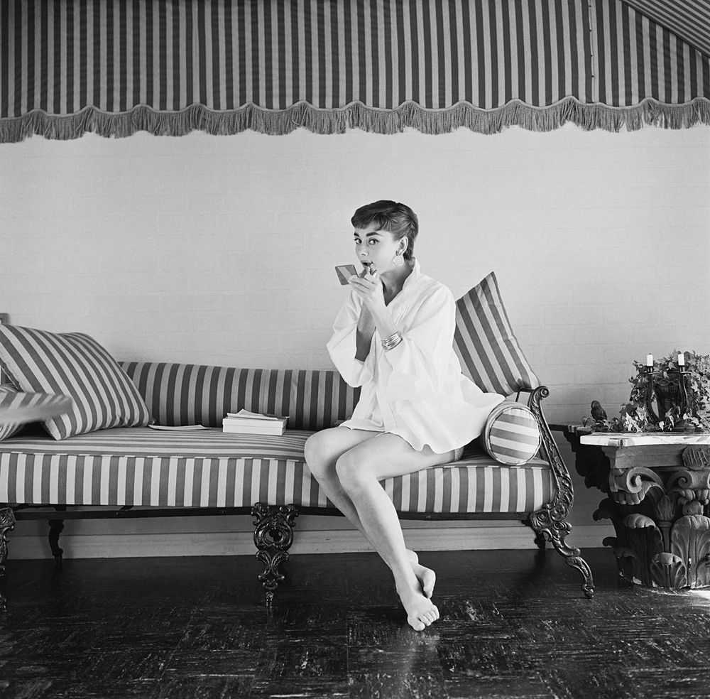 Mark Shaw, ‘Audrey Hepburn on Striped Sofa, Applies Lipstick, 1954’, 1954, Print, Pigment print on Hahnemϋhle photo rag paper, null,